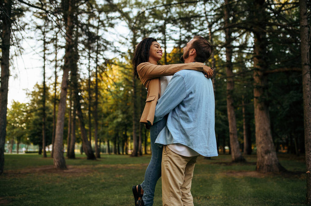 Happy love couple embracing, romantic walking in the park. Man and woman relax outdoors, green lawn on background. Family relax on the meadow in summertime, weekend in nature - Фото, зображення