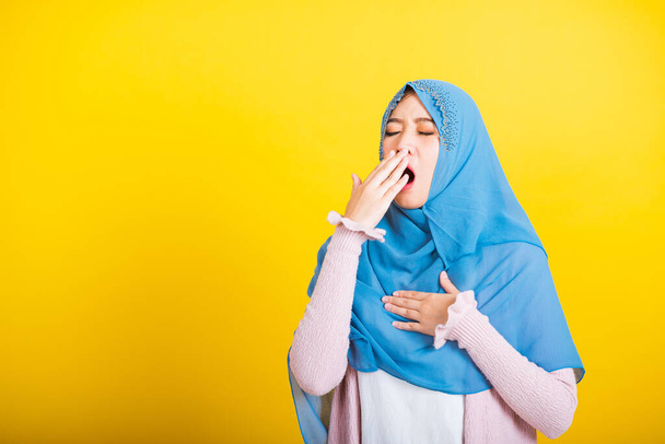 Asian Muslim Arab, Portrait of happy beautiful young woman Islam religious wear veil hijab funny she sleepy yawning wide open mouth hand cover mouth eyes closed studio shot isolated yellow background - Fotó, kép
