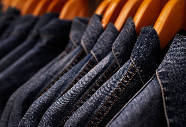 Selective focus on jacket jeans hanging on rack in clothes shop. Denim jeans with jeans pattern. Textile industry. Jeans fashion and shopping concept. Clothing concept. Denim jacket on rack for sale. - Foto, imagen