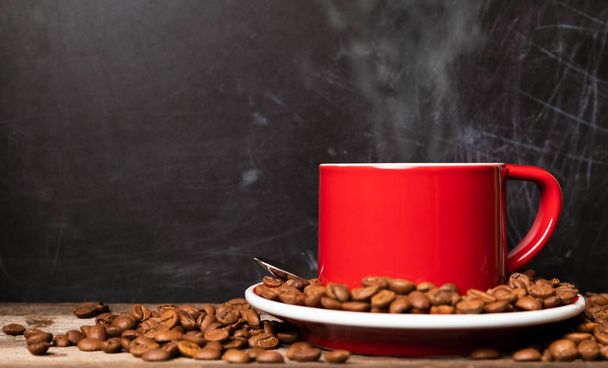 Red cup of coffee with coffee beans on dark textured background. Morning fresh energy concept. - Photo, Image