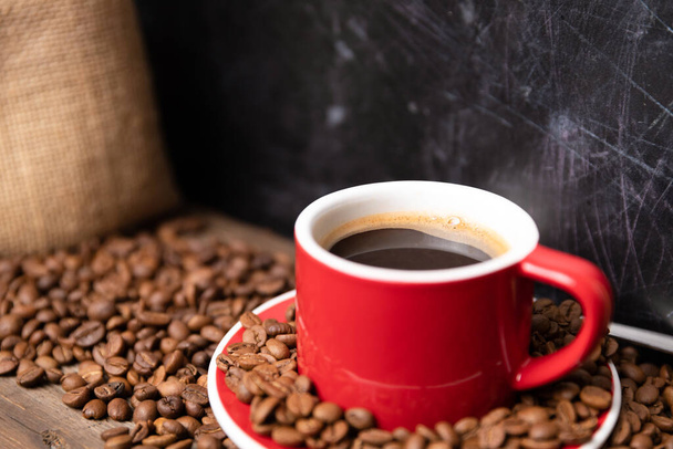 Red cup of coffee with coffee beans on dark textured background. Morning fresh energy concept. - Fotografie, Obrázek