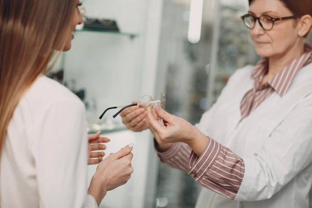 Großaufnahme einer hinreißenden jungen lächelnden Frau, die an der Optikerecke im Einkaufszentrum Gläser pflückt und auswählt. Glückliche schöne Frau kauft Brille beim Augenarzt - Foto, Bild