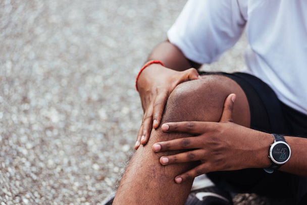 Close up Asian sport runner black man wear watch sitting he uses hands joint hold on his knee while running at the outdoor street health park, healthy exercise Injury from workout concept - Фото, зображення