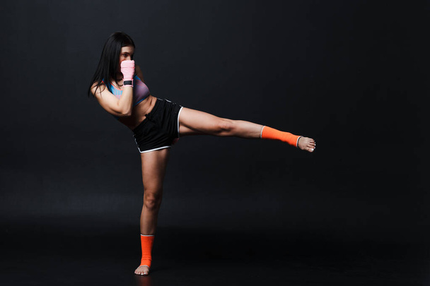 Sportsman muay thai woman boxer posing in training studio at black background. - Foto, Bild