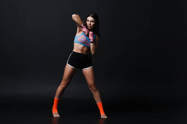 Sportsman muay thai woman boxer posing in training studio at black background. - Foto, immagini