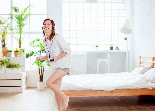excited young woman holding mobile phone singing and dancing at home - Foto, imagen