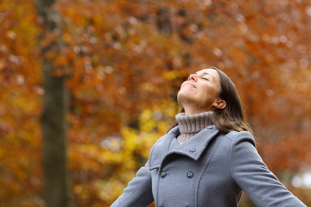 Middle age female wearing grey jacket breathing fresh air standing in a forest in fall season - Photo, Image