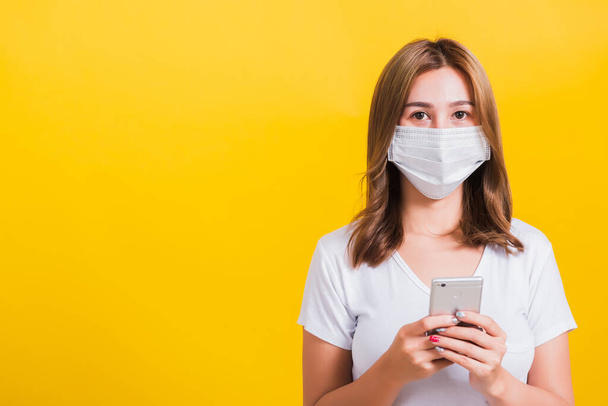 Portrait Asian Thai beautiful happy young woman wearing mask protection, reading news update on smartphone health care, studio shot isolated on yellow background, with copy space - Φωτογραφία, εικόνα