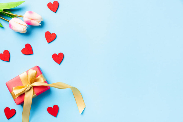 Happy Valentines' day background concept. Red gift box with a golden bow ribbon and wood red hearts composition greeting card for love isolated on blue background with copy space. Top View from above - Фото, изображение