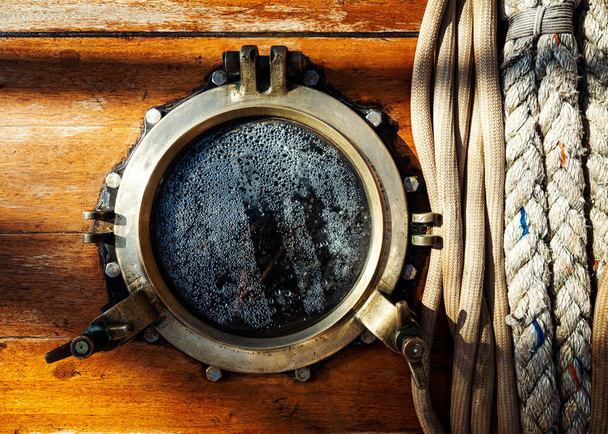 Vintage sailboat brass porthole and ropes on wooden wall. Mist on the glass window. - Fotoğraf, Görsel