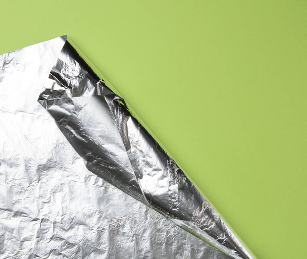 rolled sheet of foil on a green background, the corner is folded, copy space - Foto, Imagen