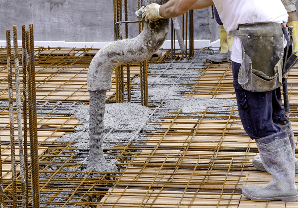 Строитель заливает цемент или бетон насосной трубой. Подробная информация о работнике и оборудовании - Фото, изображение