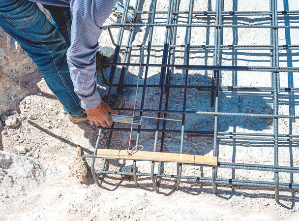 Trabalhador da construção verifica a posição das hastes de reforço de uma fundação de concreto armado com uma fita métrica. - Foto, Imagem