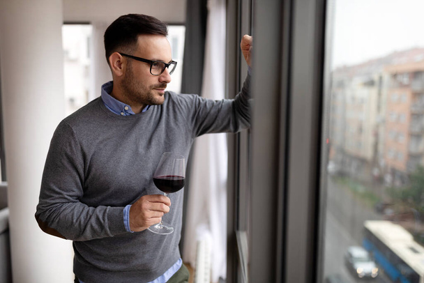 Portrait of handsome young man holding glass of red wine at home - Фото, зображення