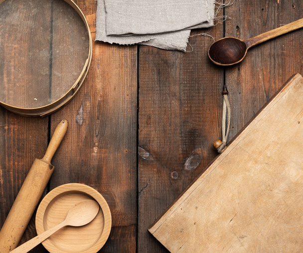very old wooden kitchen vintage items: sieve, rolling pin, empty spoons and round plates on brown wooden table, top view - Photo, image