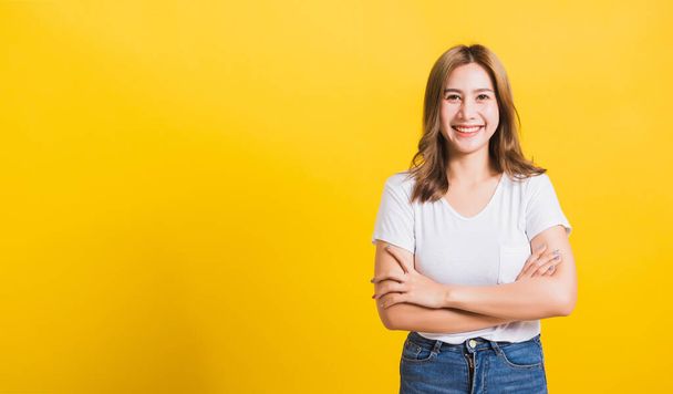 Asian Thai happy portrait beautiful cute young woman standing wear t-shirt her smile confidence with crossed arms looking to side up isolated, studio shot on yellow background and copy space - Foto, imagen
