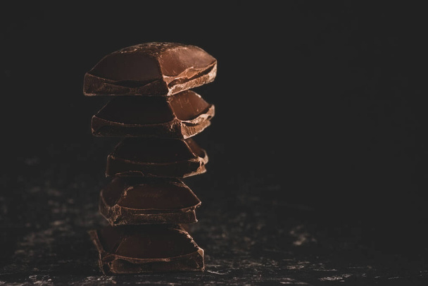 Closeup of broken dark chocolate blocks stack on black background with copy space - Foto, imagen