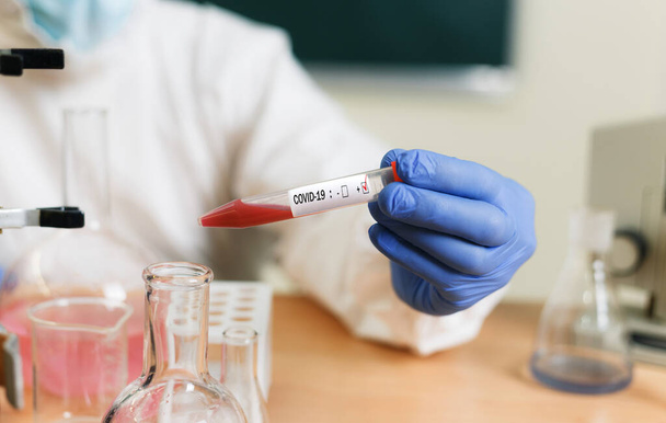 a chemical scientist in the lab wearing a white protective suit and mask carefully examines a test tube with a plasma sample. coronavirus in vitro - Foto, imagen