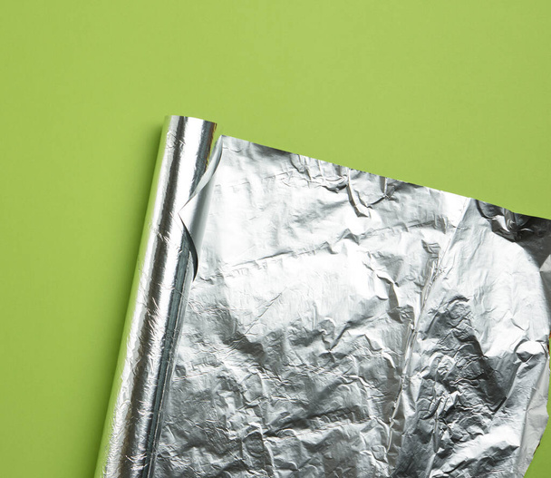 rolled sheet of foil on a green background, the corner is folded, flat lay - Foto, Bild