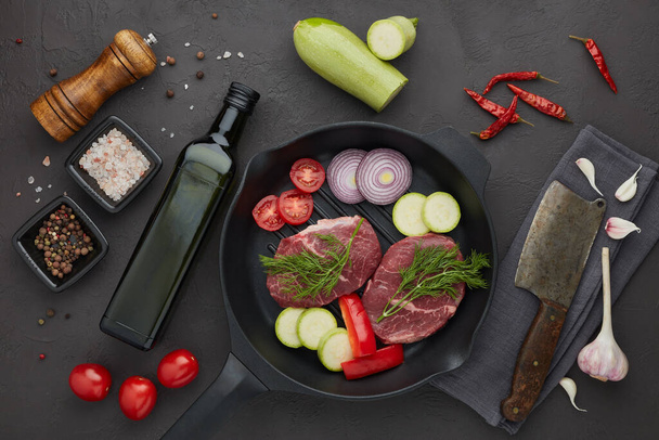Raw fresh meat and vegetables. Beef steaks and cutting vegetables on grill  pan, olive oil and spices on black slate background. Top view. Steak menu - Photo, image