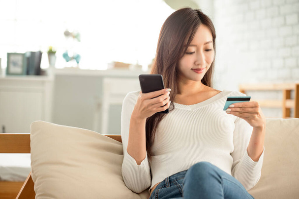 young woman buying online with  credit card and smart phone sitting on  couch at home - Photo, image