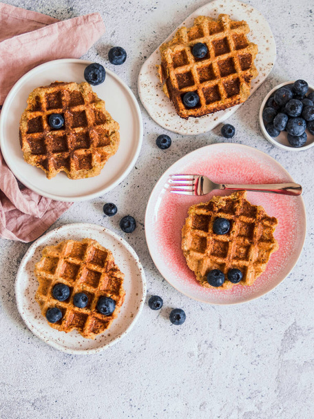 Easy healthy gluten free oat waffles with copy space. Plates with appetizing homemade waffles with oat flour decorated blueberries, on light gray cement background. Vertical. Top down view or flat lay - Fotoğraf, Görsel