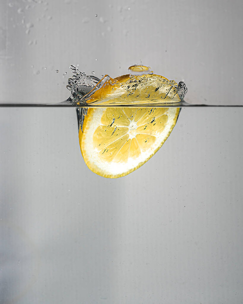 A slice of lemon drops with a splash in clear water - Foto, immagini