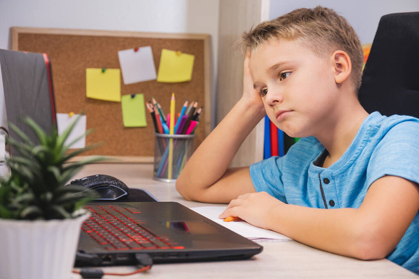 Sad schoolboy studies at home with laptop and does school homework. Home learning, online education. - Фото, зображення