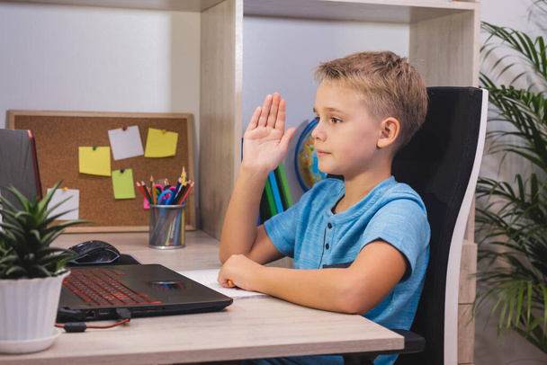Schoolboy studies at home with laptop and raised his hand to answer the question. Home learning, online education. - Photo, image