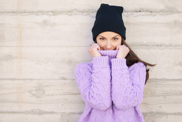 Happy young woman wearing winter hat against urban wall. - Fotoğraf, Görsel