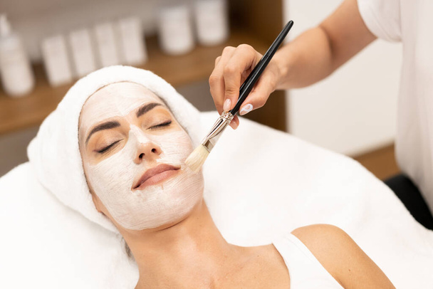Aesthetics applying a mask to the face of a Middle-aged woman in modern wellness center. - Foto, Imagem