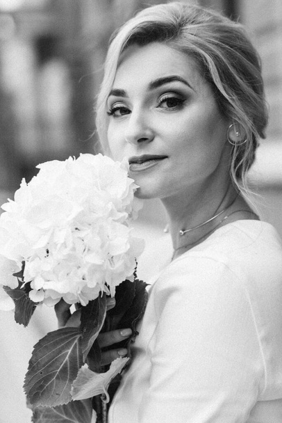 Portrait of a beautiful woman with an elegant hairstyle in a white jacket and hydrangea flowers in her hands. Soft selective focus. - Photo, Image