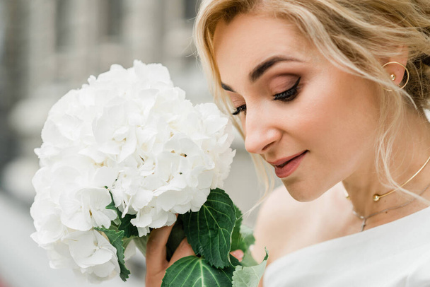 Egy gyönyörű nő portréja, elegáns frizurával, fehér kabátban és hortenzia virágokkal a kezében. Puha szelektív fókusz. - Fotó, kép