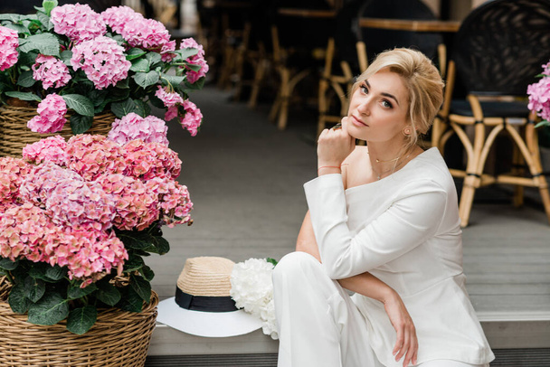 A beautiful elegant woman in a white trouser suit among the pink hydrangeas. Soft selective focus. - Foto, imagen
