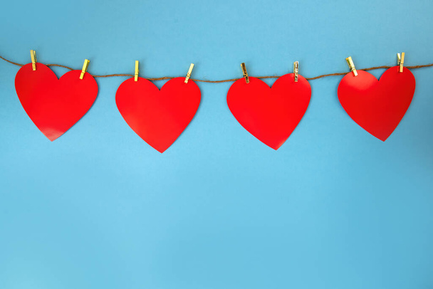 Four red hearts hanging on cord attached by golden pins on blue background. Symbol of love on colorful backdrop with copy space. Love sign for valentine with space for text. - Foto, Imagen