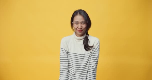 Positieve vrolijke jonge mooie Asia vrouw met donker haar in casual kleding glimlachend kijkend naar camera staan geïsoleerd over gele achtergrond. Positief gevoel goed humeur concept. - Video