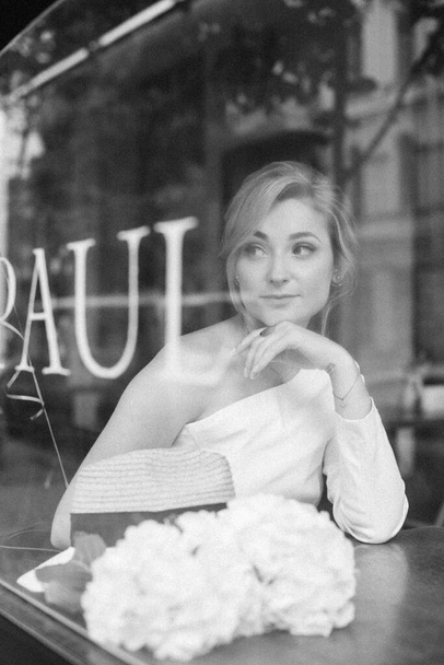A well thought-out concept. Beautiful elegant woman in a cafe, looks through the window glass. Soft selective focus. - Photo, Image