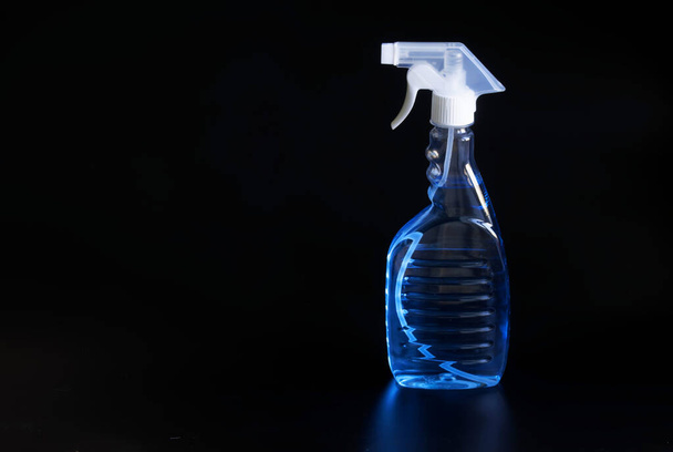 El recipiente transparente con una botella de aerosol y un líquido desinfectante azul claro se coloca sobre un fondo negro. El concepto de limpieza de gérmenes y virus y desinfección. Primer plano - Foto, Imagen