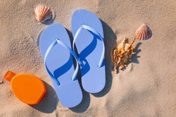 Stylish flip flops, sunscreen and sea shells on beach, flat lay - 写真・画像