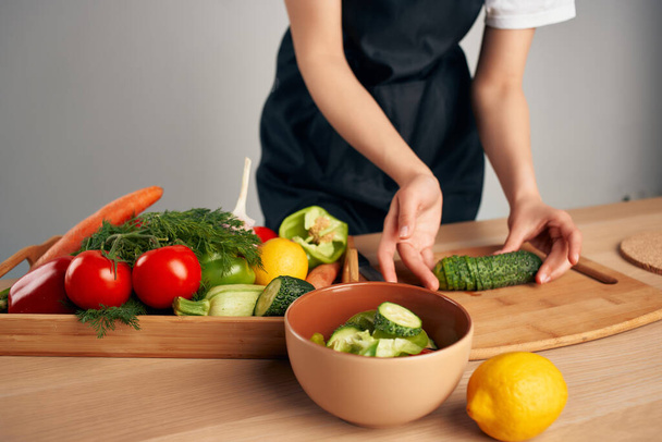 ama de casa en un delantal negro en la cocina cocina cocina vitaminas ensalada - Foto, imagen