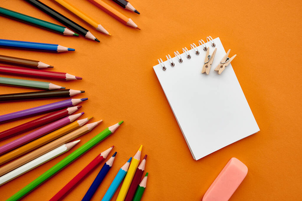 Zestaw kolorowych ołówków i notatnika, pomarańczowe tło. Artykuły biurowe, akcesoria szkolne lub edukacyjne, narzędzia do pisania i rysowania - Zdjęcie, obraz