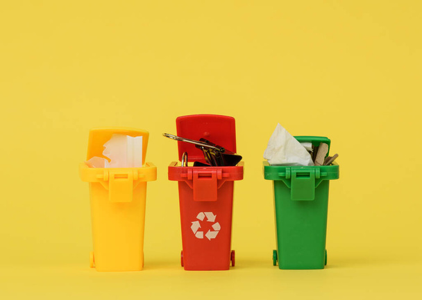drie veelkleurige plastic containers op een gele achtergrond, het concept van het correct sorteren van afval voor verdere recycling - Foto, afbeelding