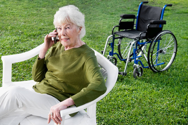 senior woman talking on mobile phone and smiling while sitting on bench in park - Fotoğraf, Görsel