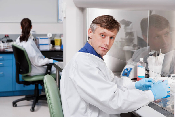 νεαρός άνδρας γιατρός σε ένα λευκό παλτό και μπλε γάντια εργάζεται σε ένα εργαστήριο. - Φωτογραφία, εικόνα