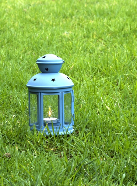 синій ліхтар, з палаючої свічки всередині, зелена трава  - Фото, зображення