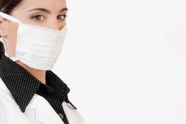portrait of a young woman in a white coat and a protective mask on a gray background - Фото, изображение