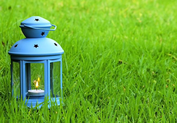 Linterna azul, con vela encendida en el interior, sobre hierba verde
  - Foto, Imagen