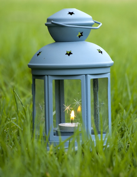 Linterna azul, con vela encendida en el interior, sobre hierba verde
  - Foto, Imagen