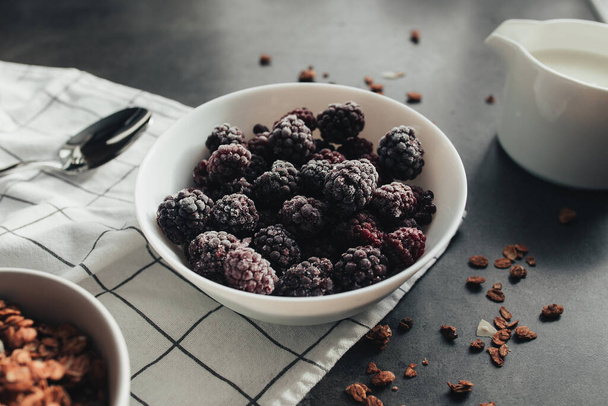 Frozen blackberries, granola, cream, towel on table. Blurred background. High quality photo - 写真・画像