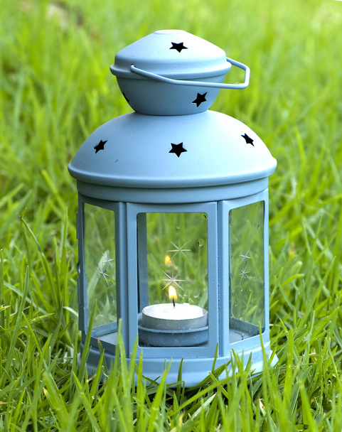 niebieskim latarnią, z płonącą świecą wewnątrz, na zielonej trawie  - Zdjęcie, obraz